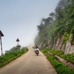 Motocyklista jedzie we mgle krętą górską drogą nad stromymi urwiskami