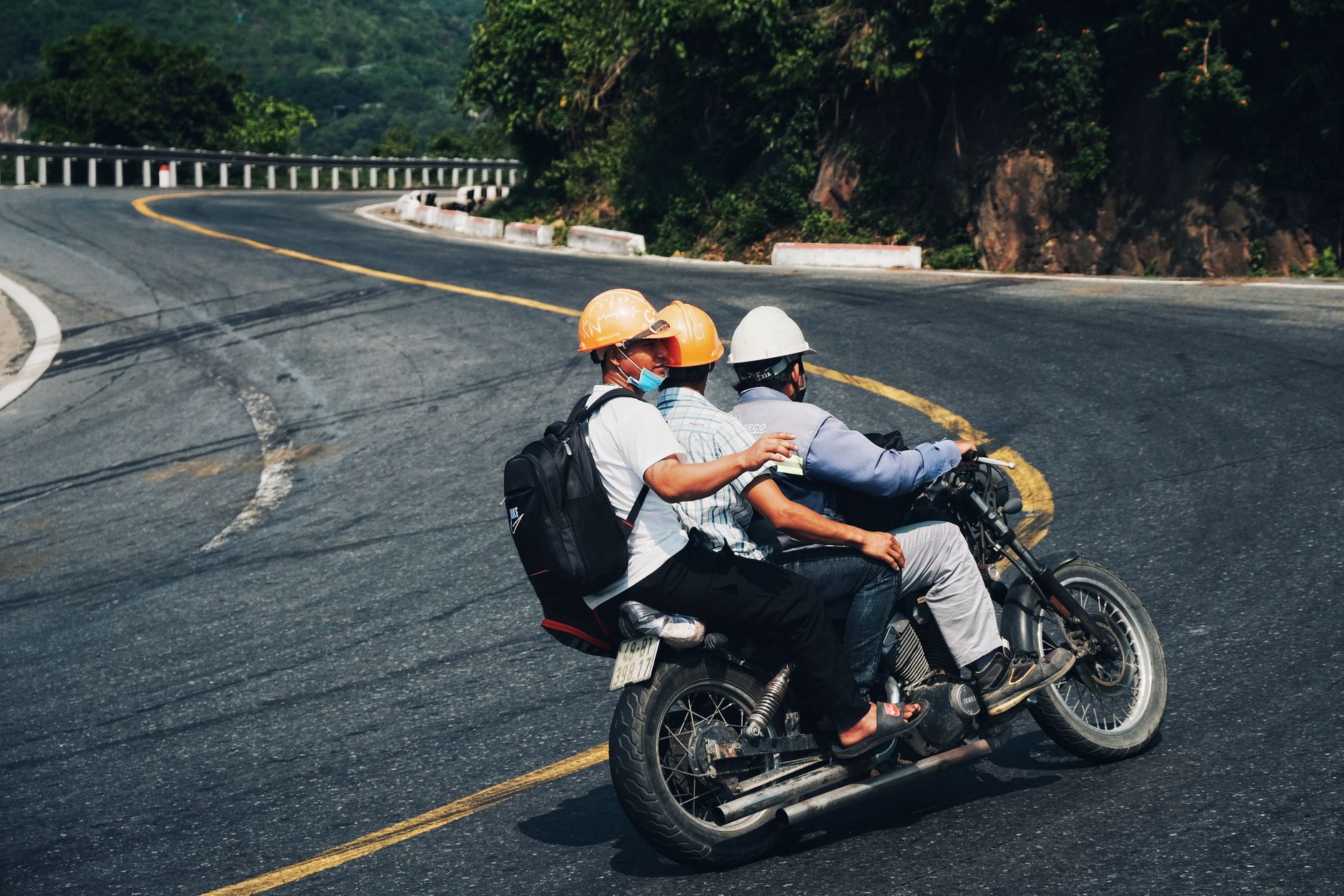 Trzech motocyklistów w kaskach jedzie krętą górską drogą