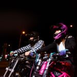 Dwóch motocyklistów jedzie nocą przez miasto w neonowych światłach