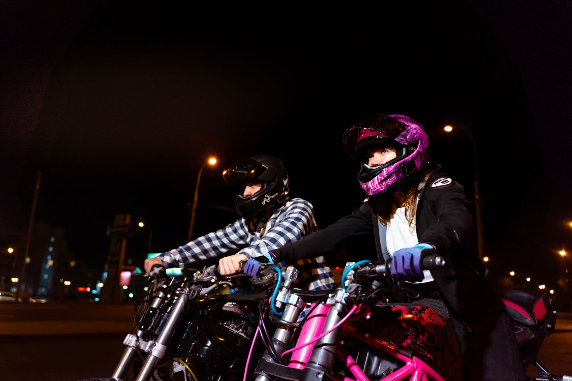 Dwóch motocyklistów jedzie nocą przez miasto w neonowych światłach