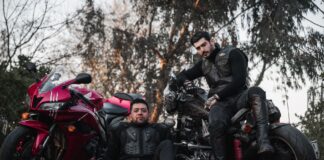 Dwóch motocyklistów w kombinezonach pozuje przy motocyklach na zewnątrz