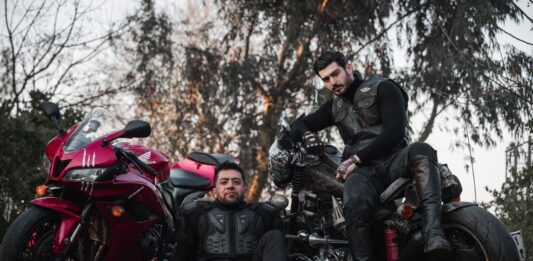Dwóch motocyklistów w kombinezonach pozuje przy motocyklach na zewnątrz