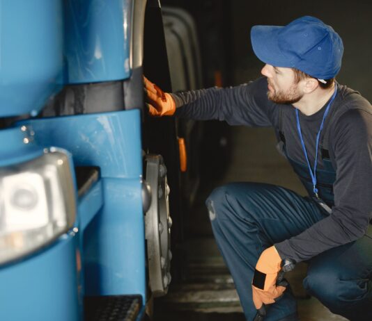 Jak bezpiecznie kupić używaną ciężarówkę z importu: praktyczny poradnik dla firm transportowych Mechanik w warsztacie sprawdza koło niebieskiej ciężarówki
