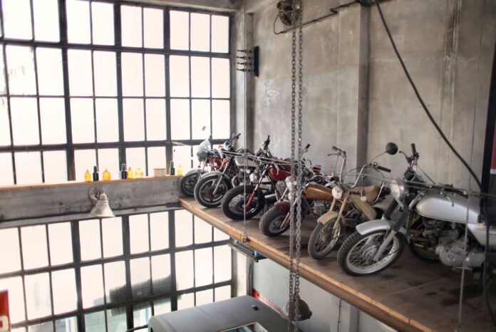 Rząd retro motocykli na podestach w garażu przy dużych oknach Rząd retro motocykli na podestach w garażu przy dużych oknach