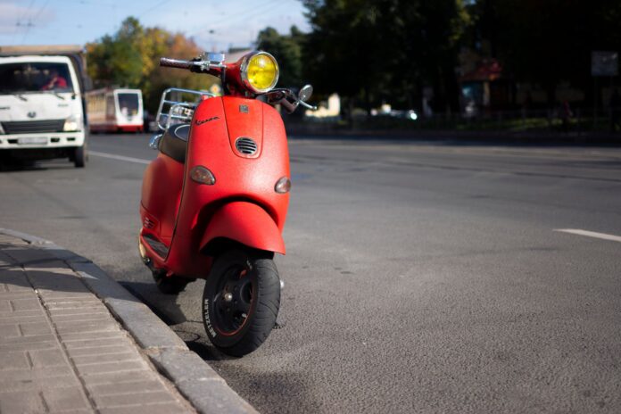 Czerwony skuter Vespa zaparkowany przy miejskiej ulicy Czerwony skuter Vespa zaparkowany przy miejskiej ulicy