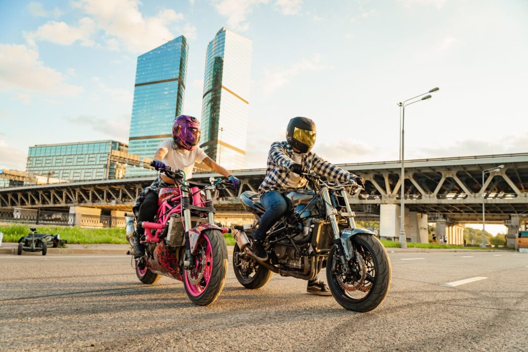 Dwóch motocyklistów jedzie między miejskimi wieżowcami o zachodzie słońca Dwóch motocyklistów jedzie między miejskimi wieżowcami o zachodzie słońca