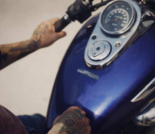 Paliwo E10 a zimowanie motocykla – czy warto lać stabilizator i tankować benzynę 98 do pełna? Wytatuowane dłonie motocyklisty na kierownicy motocykla